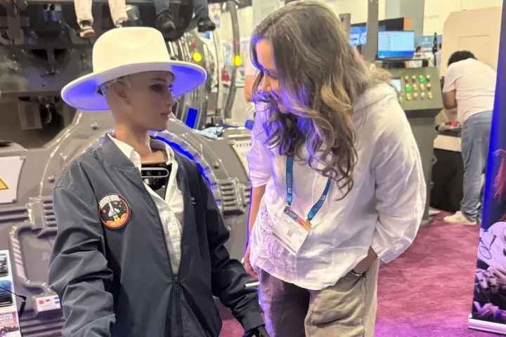 Zeynep A. Talu-Balci interacts with Sophia the Robot at the DOF Robotics booth during Seatrade Cruise Global 2025 in Miami Beach. Sophia, a humanoid robot developed by Hanson Robotics, is known for her expressive face and conversational AI. The setting features immersive tech displays highlighting the future of entertainment and guest experiences.